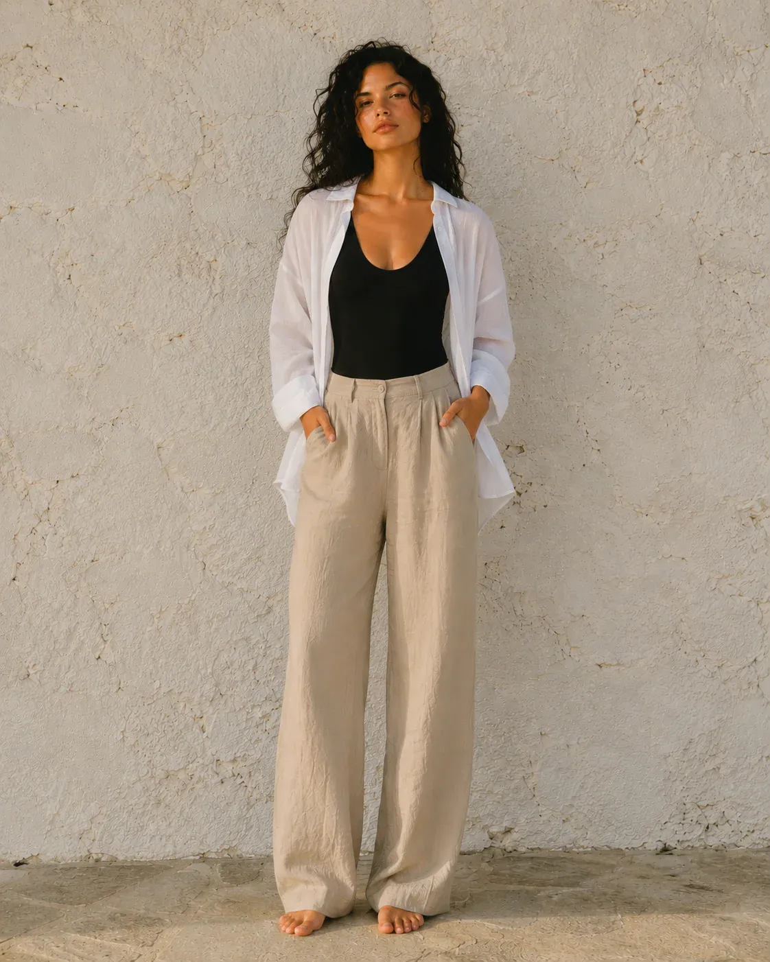 A woman facing the camera in a white shirt over a black top by a stone wall.